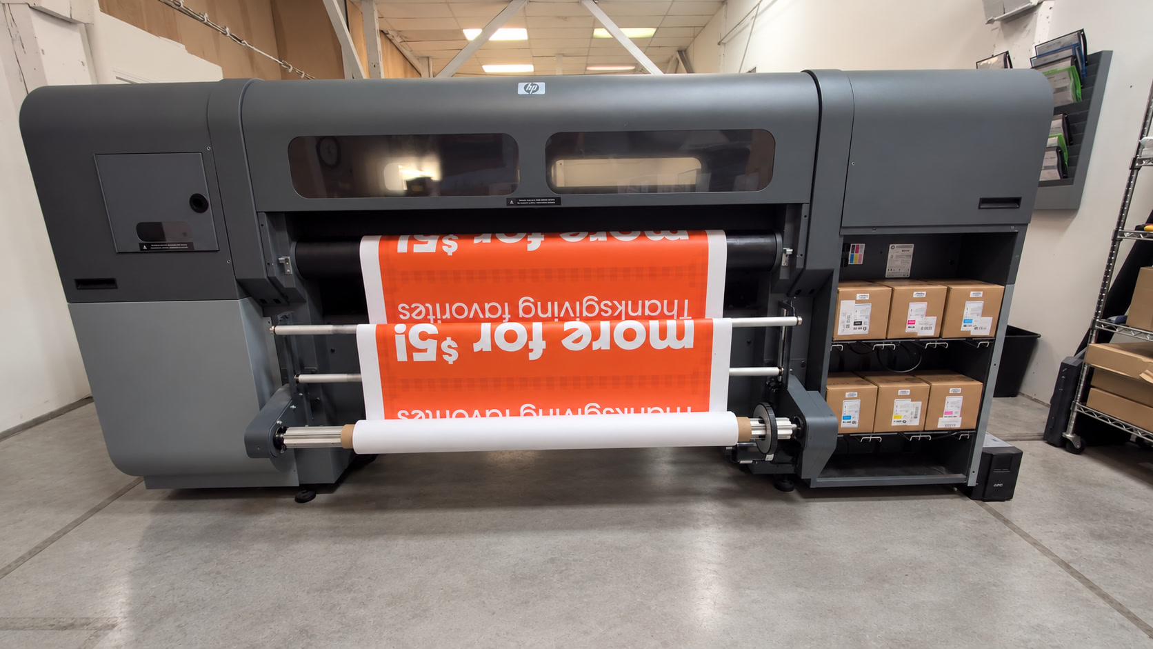 HP flatbed/hybrid printer producing orange signage, with a clean concrete floor and tidy ink box labels